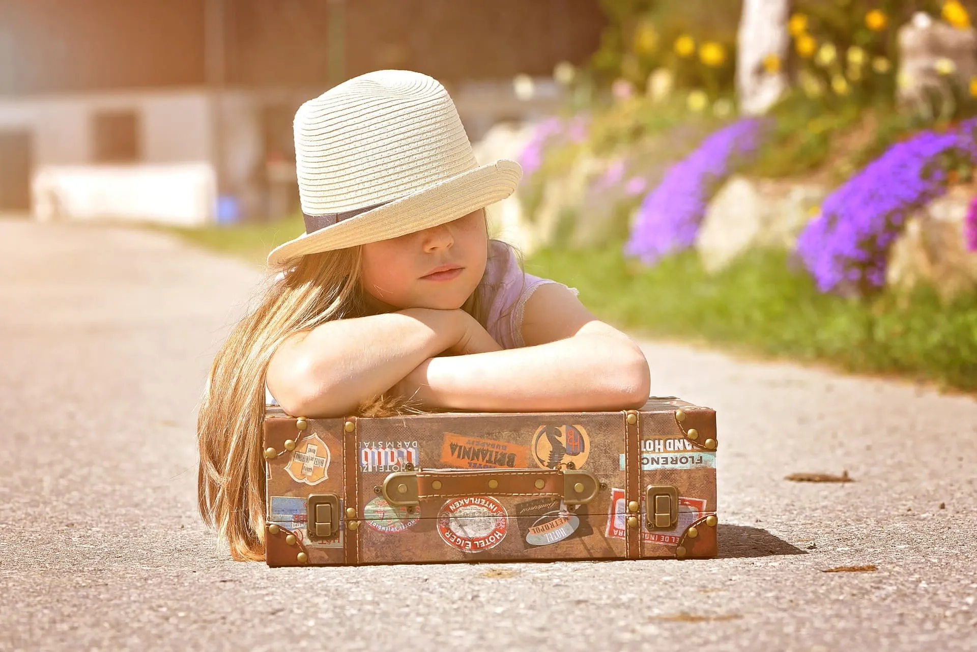 Kind mit Sonnenhut sitzt auf einem alten Koffer – bereit für den Weg zur Schule